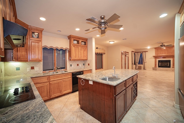 kitchen with sink, a tile fireplace, ceiling fan, black appliances, and an island with sink