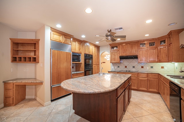 kitchen with a center island with sink, light stone countertops, black appliances, light tile patterned flooring, and decorative backsplash