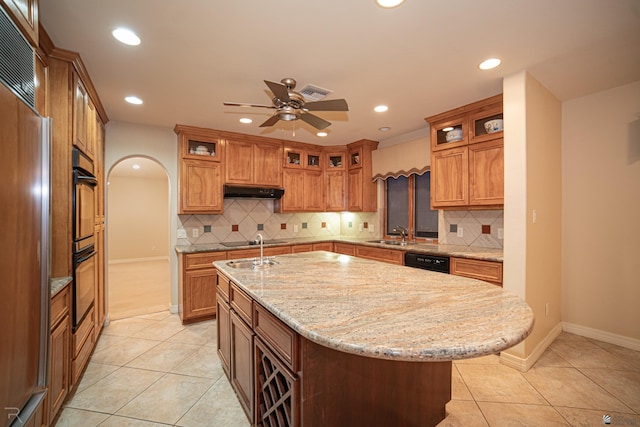 kitchen featuring light tile patterned flooring, a kitchen island with sink, light stone counters, and black appliances