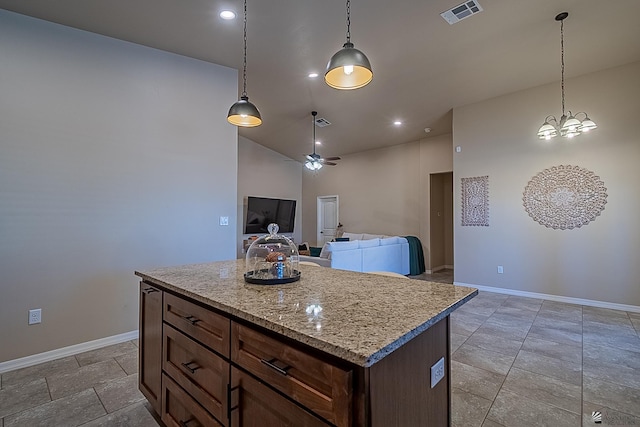 kitchen with decorative light fixtures, light stone countertops, ceiling fan, and a kitchen island