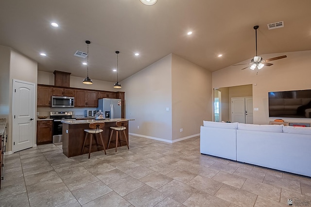 kitchen featuring pendant lighting, a breakfast bar, appliances with stainless steel finishes, light stone countertops, and an island with sink