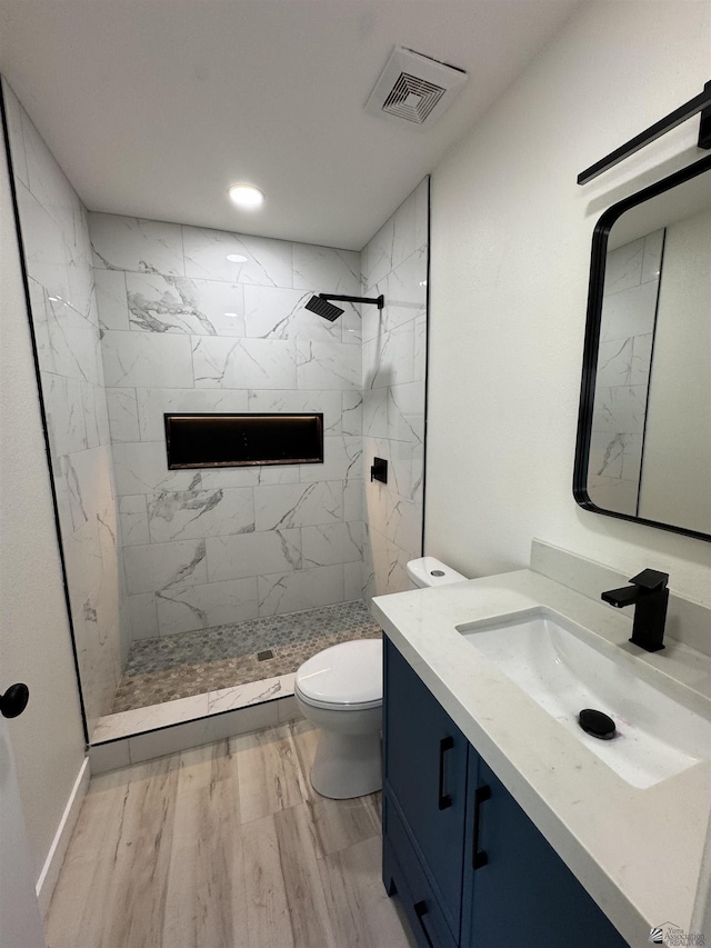 bathroom with visible vents, toilet, a tile shower, wood finished floors, and vanity