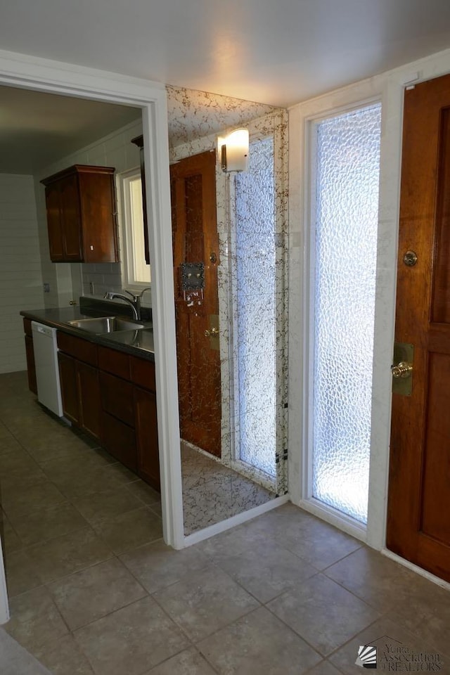 kitchen with a sink, dark countertops, white dishwasher, and light tile patterned floors