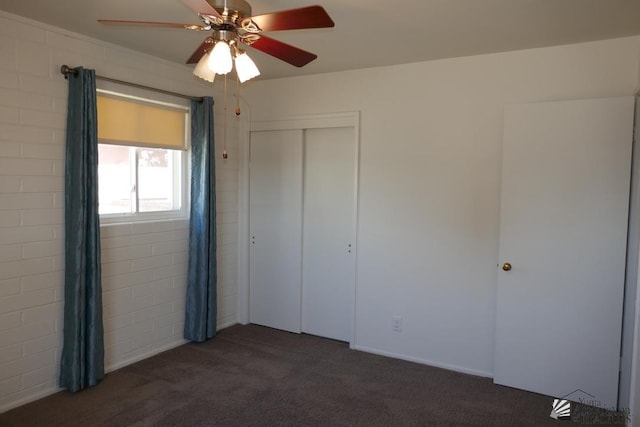 unfurnished bedroom featuring dark colored carpet, a closet, and a ceiling fan