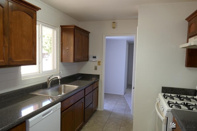 kitchen featuring white appliances, light tile patterned floors, a sink, under cabinet range hood, and dark countertops