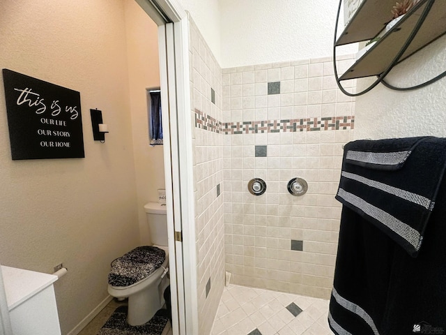 bathroom with a tile shower, toilet, and a textured wall