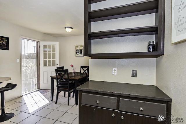 kitchen with dark countertops, light tile patterned floors, dark brown cabinetry, and open shelves