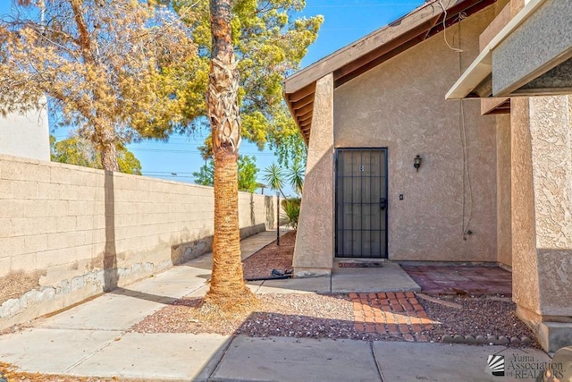 view of exterior entry featuring fence, a patio, and stucco siding