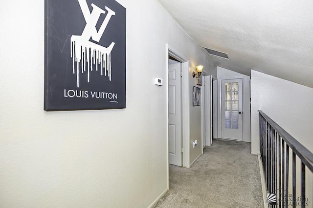 hallway featuring lofted ceiling, light colored carpet, visible vents, and a textured ceiling