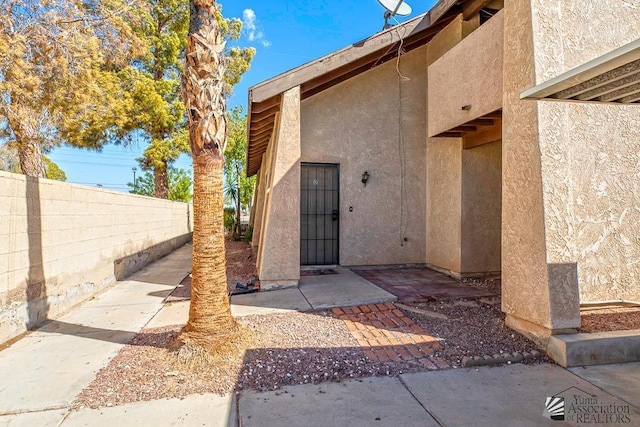 view of exterior entry with fence, a patio, and stucco siding