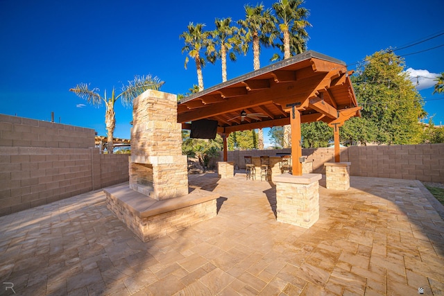 view of patio / terrace with ceiling fan, a gazebo, an outdoor stone fireplace, and a bar