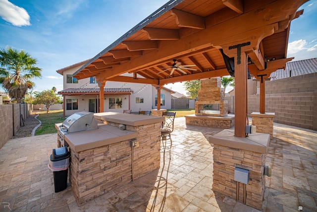 view of patio / terrace featuring ceiling fan, an outdoor stone fireplace, a bar, grilling area, and exterior kitchen