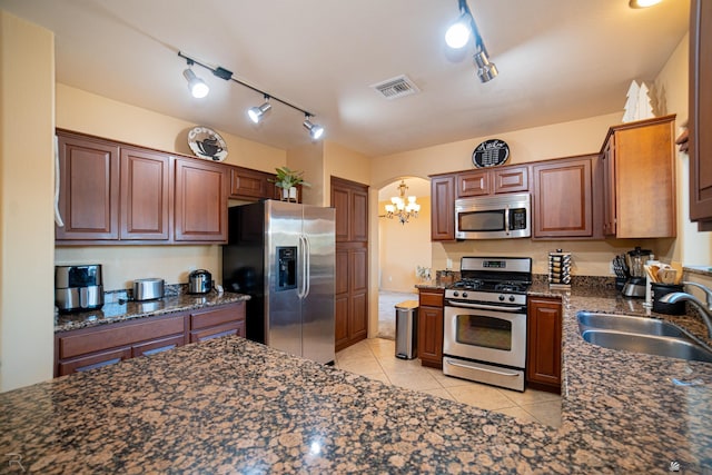 kitchen featuring sink, dark stone countertops, light tile patterned floors, stainless steel appliances, and track lighting