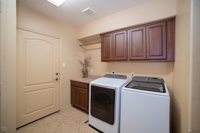 clothes washing area featuring cabinets, light tile patterned floors, and washing machine and clothes dryer