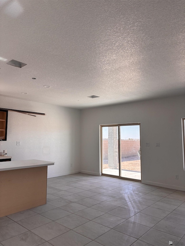 interior space with a barn door, a textured ceiling, baseboards, and light tile patterned floors