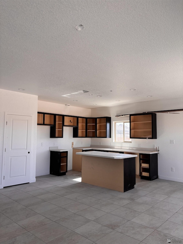 kitchen with a center island, light countertops, a textured ceiling, and open shelves