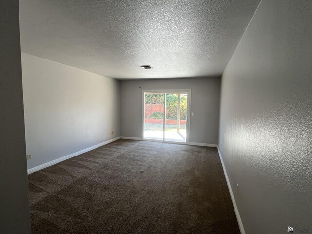 empty room with dark carpet and a textured ceiling