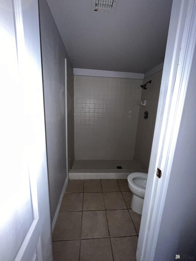 bathroom with toilet, tile patterned flooring, and tiled shower