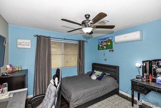 bedroom featuring a wall unit AC, a ceiling fan, a textured ceiling, wood finished floors, and baseboards