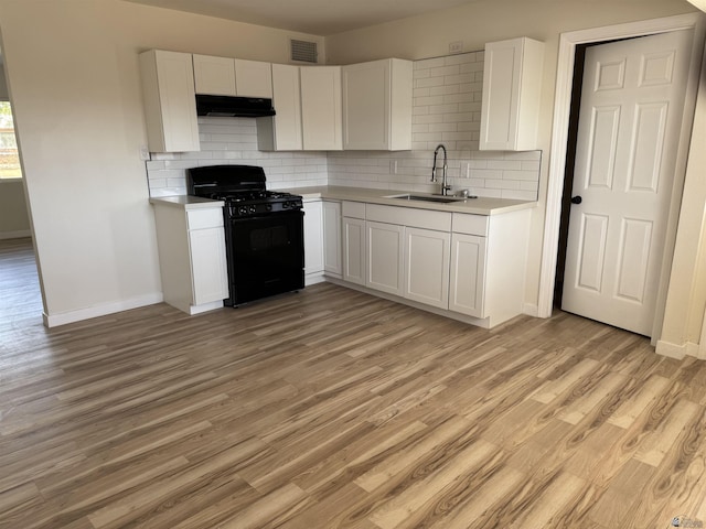 kitchen with tasteful backsplash, sink, white cabinets, gas stove, and light hardwood / wood-style flooring