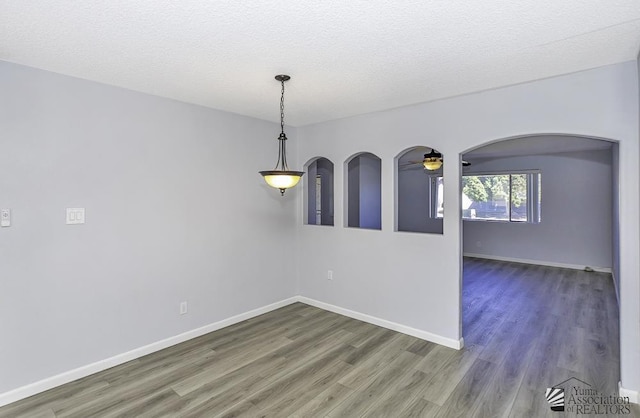 empty room with arched walkways, dark wood-style flooring, a ceiling fan, and baseboards