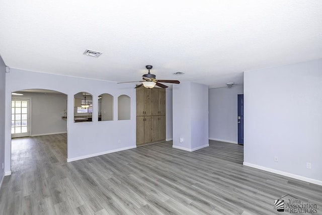 unfurnished living room with light wood finished floors, visible vents, arched walkways, and baseboards