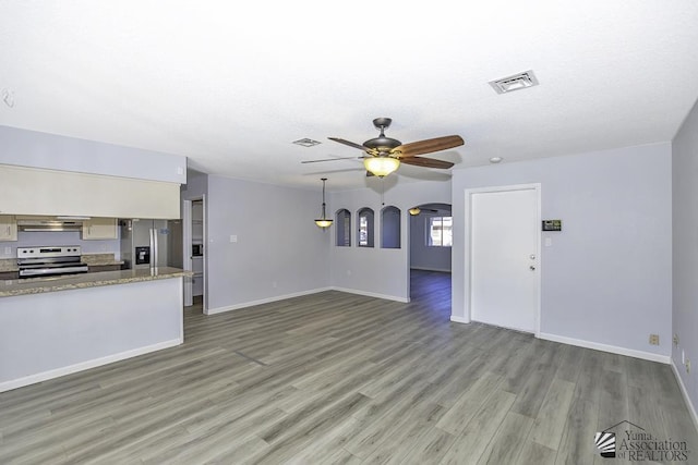 unfurnished living room featuring a ceiling fan, arched walkways, visible vents, and light wood-style floors