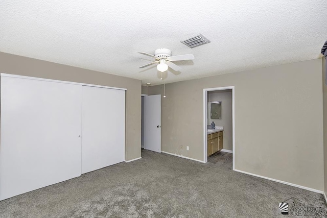 unfurnished bedroom with a textured ceiling, visible vents, a ceiling fan, a closet, and dark colored carpet