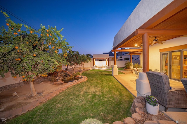 yard at dusk featuring a patio and ceiling fan