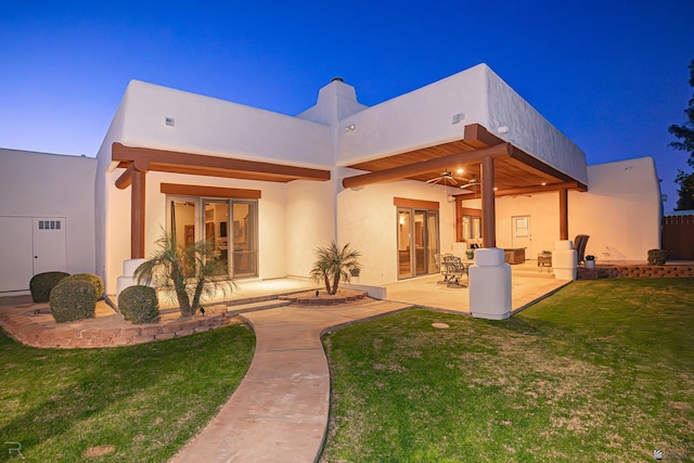 back house at dusk with a lawn, a patio, and ceiling fan