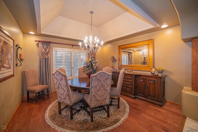 dining space with hardwood / wood-style floors, a tray ceiling, and a notable chandelier