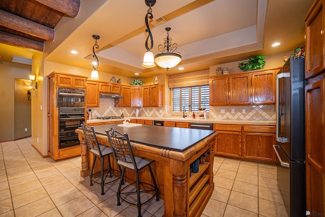 kitchen with a breakfast bar, a center island, a tray ceiling, black appliances, and decorative light fixtures