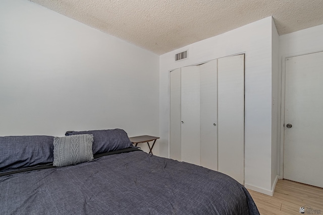 bedroom with light wood-type flooring, a textured ceiling, and a closet