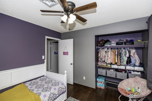 bedroom featuring ceiling fan, a textured ceiling, a wainscoted wall, wood finished floors, and a closet