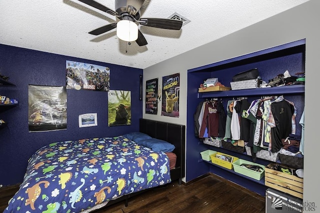 bedroom with a ceiling fan, visible vents, a textured ceiling, and wood finished floors