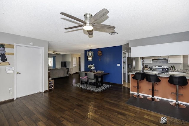 interior space featuring appliances with stainless steel finishes, dark wood-type flooring, a breakfast bar, and under cabinet range hood