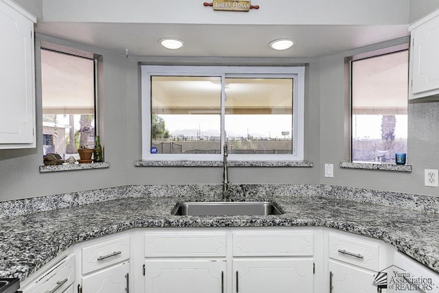 kitchen with dark stone counters, a sink, white cabinetry, and recessed lighting