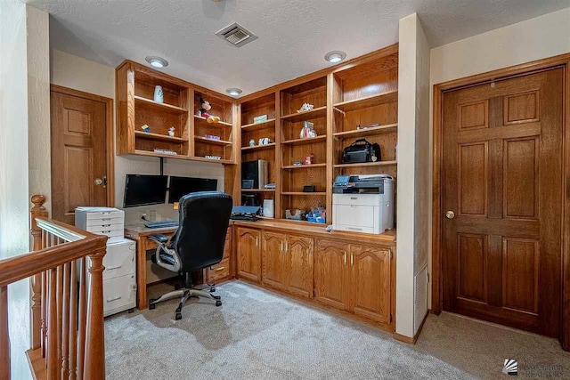 carpeted office space with built in desk and a textured ceiling