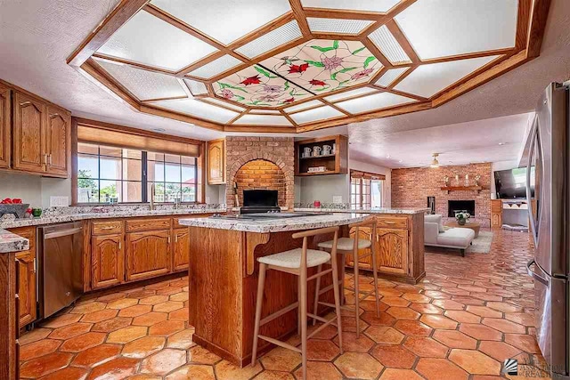 kitchen featuring a breakfast bar, a center island, a brick fireplace, ceiling fan, and stainless steel appliances