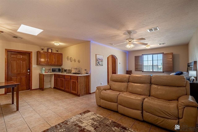 tiled living room featuring a textured ceiling, a skylight, and ceiling fan