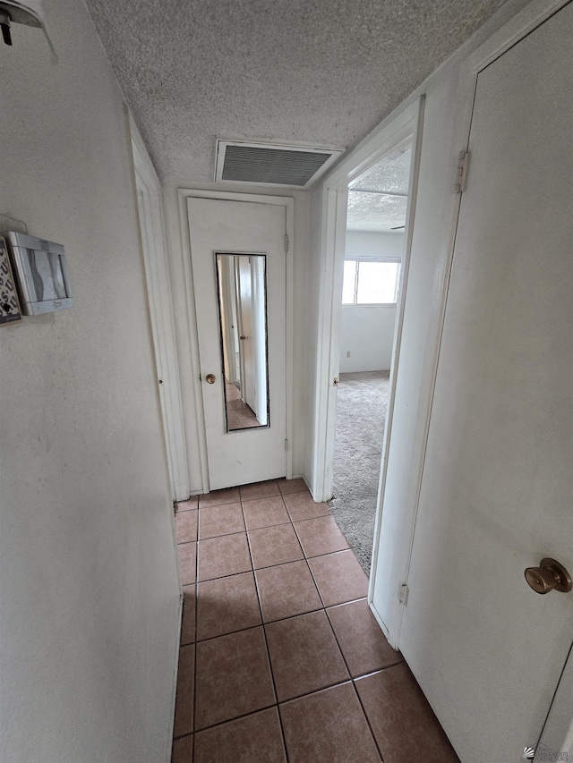 hall featuring light tile patterned flooring and a textured ceiling