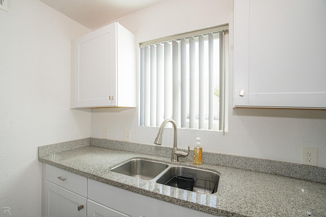 kitchen featuring white cabinetry, light stone counters, and sink