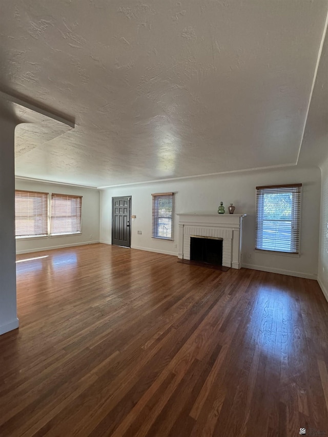 unfurnished living room featuring a wealth of natural light, a textured ceiling, a brick fireplace, and dark wood-style floors