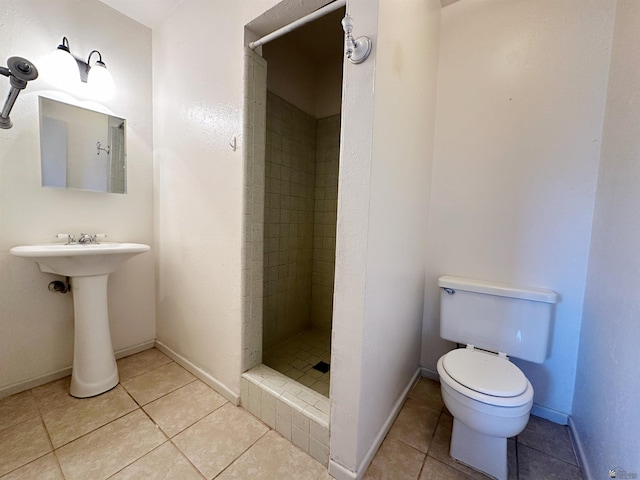 bathroom with tile patterned flooring, a tile shower, toilet, and sink