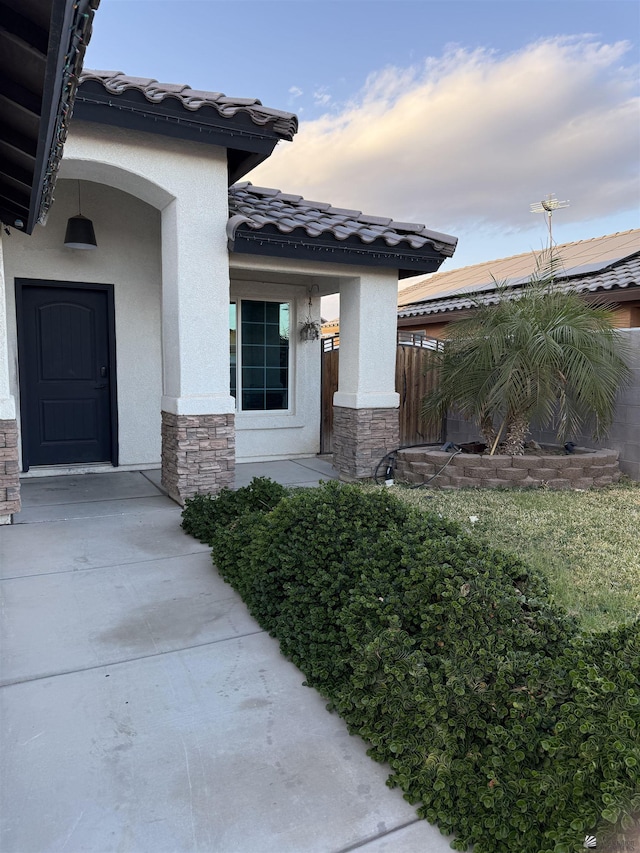 doorway to property featuring stone siding, fence, a tiled roof, and stucco siding