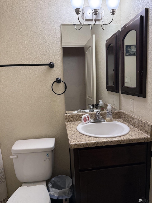 bathroom with toilet, a textured wall, a notable chandelier, and vanity