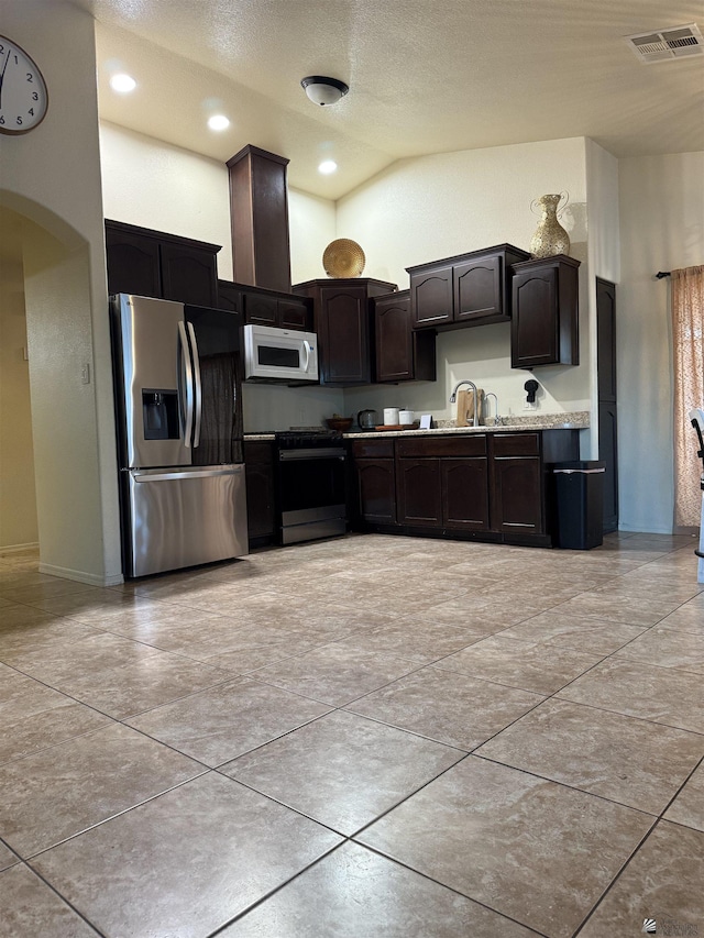 kitchen featuring high vaulted ceiling, dark brown cabinetry, stainless steel appliances, a sink, and visible vents