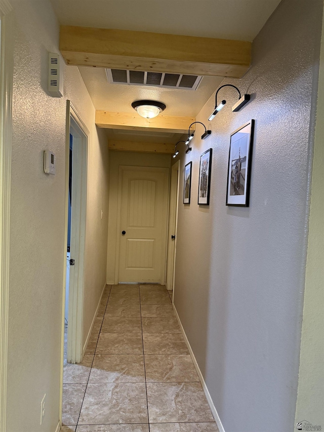 hallway with visible vents, beamed ceiling, baseboards, and light tile patterned flooring