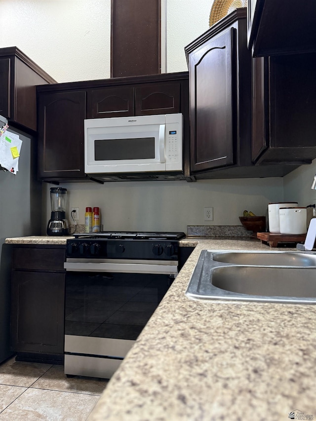 kitchen with light countertops, white microwave, freestanding refrigerator, stainless steel gas stove, and dark brown cabinetry