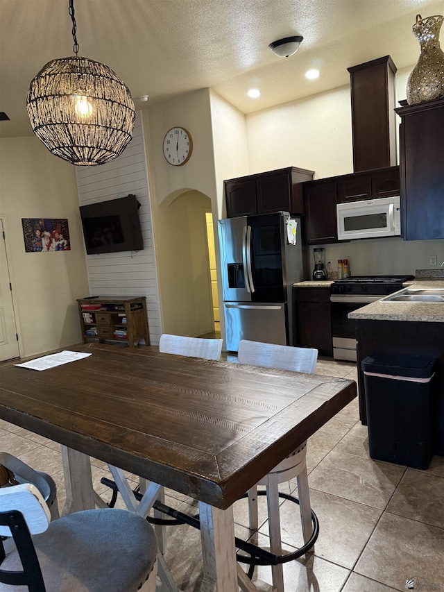 kitchen with arched walkways, appliances with stainless steel finishes, decorative light fixtures, light countertops, and a sink